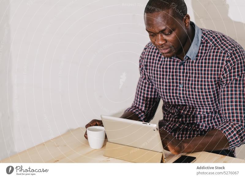 Concentrated Black Man Working with a Digital Tablet on a Wooden Table adult african black business businessman confident digital handsome happy hipster job