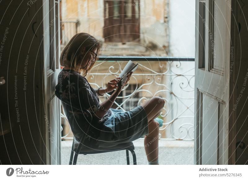 Focused woman reading book on balcony doorway travel literature hobby novel bookworm calm female young casual cuba holiday tourism idyllic summer harmony