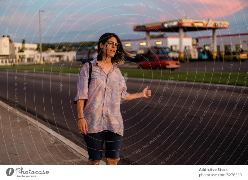 Young hitchhiking female traveler catching car on road woman hitchhike thumb up sunset evening twilight sundown calm dusk sky young casual show sign cuba