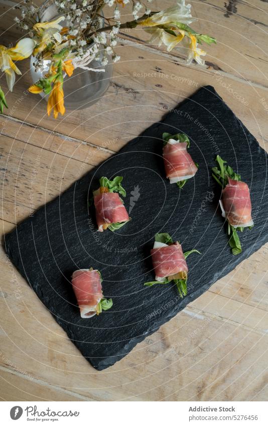 Fresh appetizer on black board near bouquet of flowers food tuna roll serve fish cuisine blossom vase bloom bunch plant dish tasty delicious fresh natural