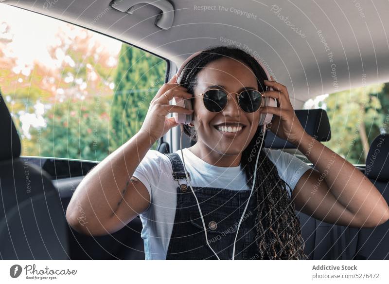 Smiling black woman in headphones smile cheerful car listen music using passenger sunglasses happy ethnic female african american young backseat device