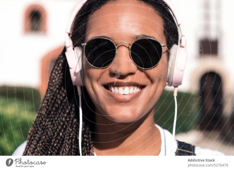 Cheerful ethnic woman in sunglasses and headphones smile cheerful portrait music listen song street accessory braid using african american style black happy