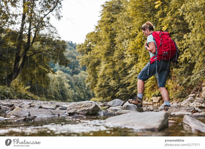 Traveling with backpack concept image. Backpacker female in trekking boots crossing mountain river. Summer vacation trip adventure travel hiking landscape