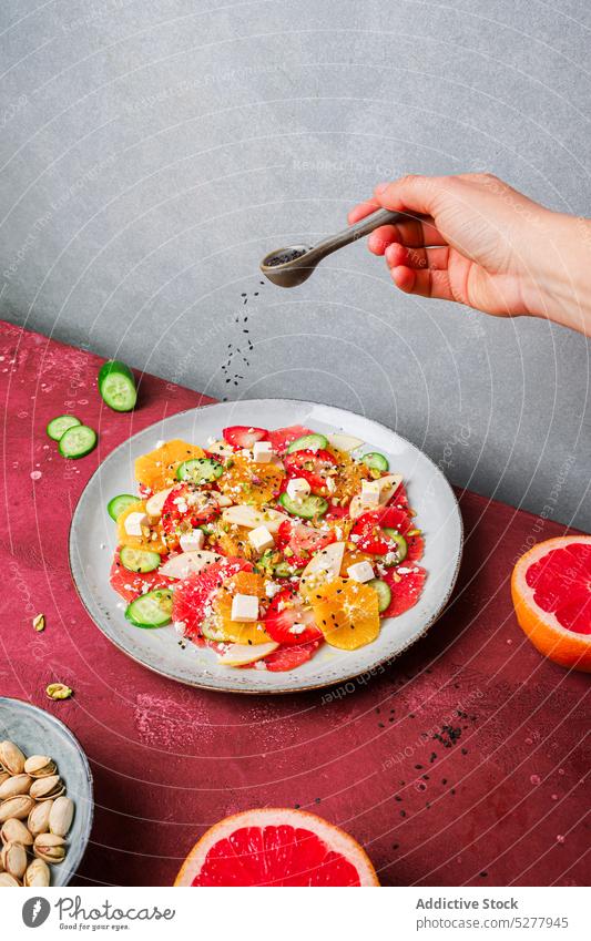 Crop person adding seeds to salad chia spoon cheese orange strawberry cucumber plate healthy fruit healthy food delicious recipe gastronomy fresh serve organic