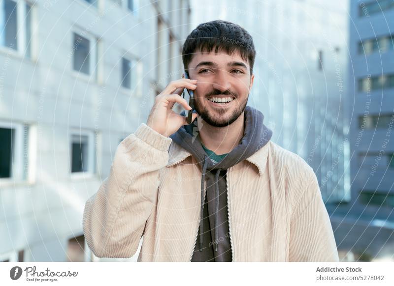 Smiling guy talking on smartphone in city man using phone call conversation speak street urban discuss smile positive male young mobile cellphone gadget