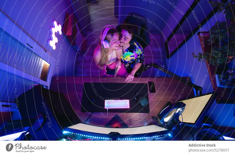 Happy couple playing video game together happy cheerful computer home relationship love neon online stream hug using device gadget boyfriend modern girlfriend
