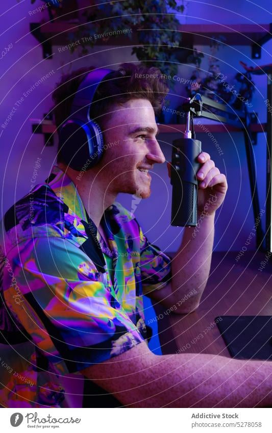 Cheerful man recording podcast in studio smile cheerful microphone headphones neon entertain radio young illuminate table male dark host gadget modern headset