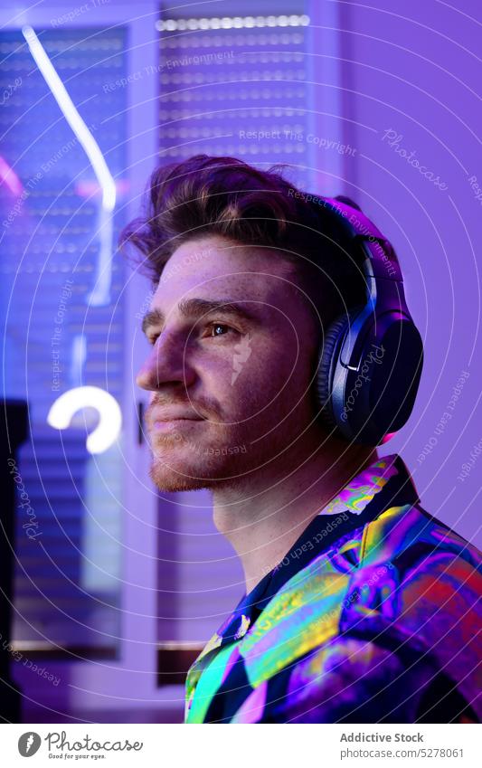 Thoughtful man in headphones looking away dreamy thoughtful portrait neon music wireless style colorful light male young listen device gadget modern illuminate