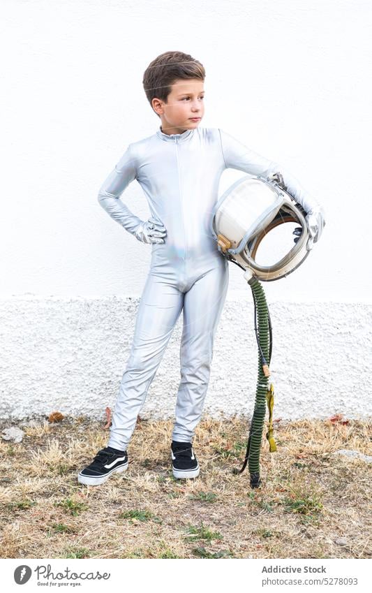 Kid in space suit holding helmet in countryside boy child cosmonaut astronaut spacesuit spaceman explorer futuristic dream costume future kid stand preteen