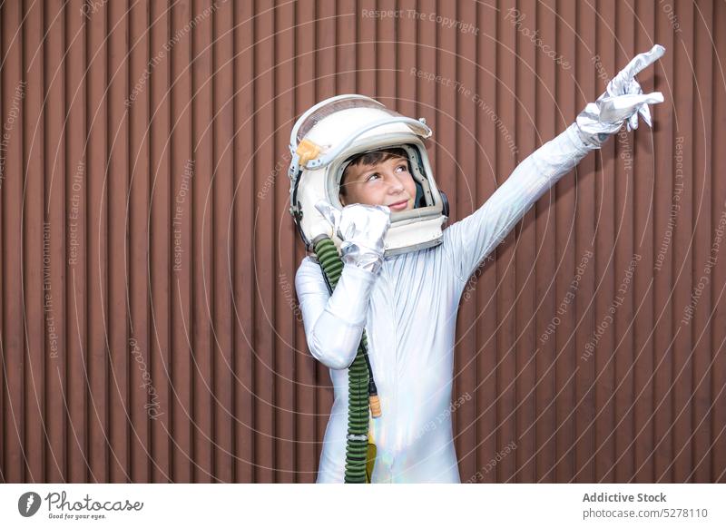 Boy in space suit against brown wall boy child cosmonaut astronaut attention explore curious show kid spacesuit surprise stand preteen interest helmet