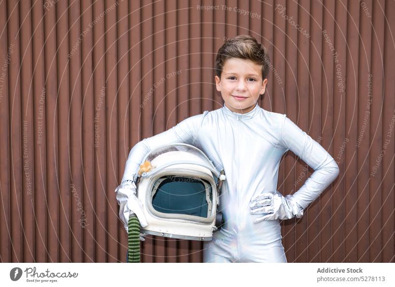 Kid in space suit standing against brown wall boy child cosmonaut astronaut spacesuit spaceman kid explorer helmet grass wither futuristic costume future