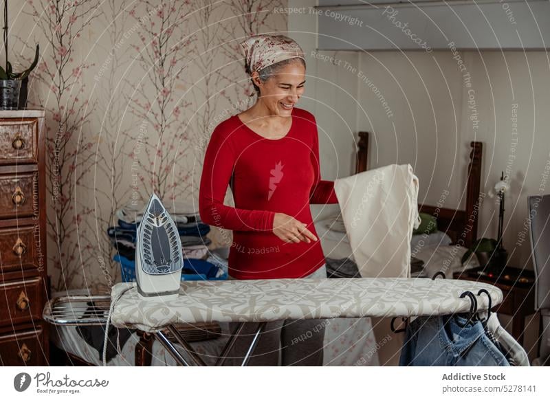 Smiling elderly woman ironing pants household housewife chore domestic home trousers housework smile routine cloth mature female casual cheerful happy