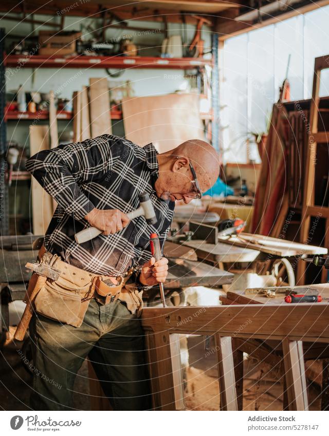 Senior carpenter using chisel and hammer in workshop man woodworker cut craftsman plank skill artisan carpentry male tool instrument equipment process manual