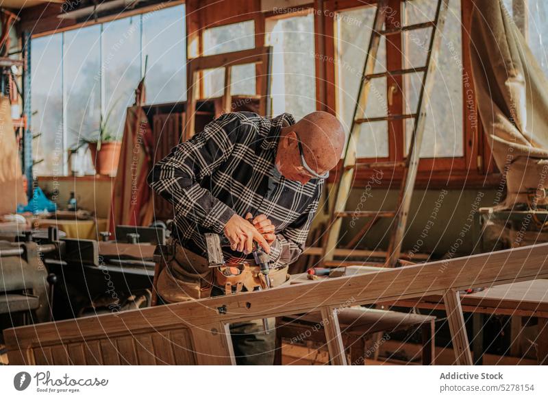 Woodworker drilling wooden plank in joinery man carpenter woodworker workshop professional carpentry male craftsman senior lumber timber artisan job instrument