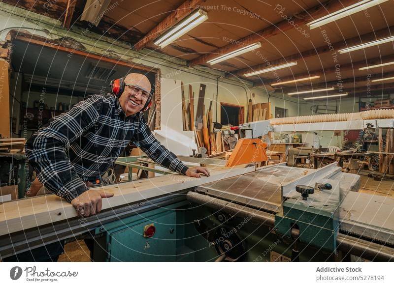 Carpenter cutting wood on circular saw table man carpenter woodwork joinery plank woodworker headphones workshop concentrate craft skill goggles male focus