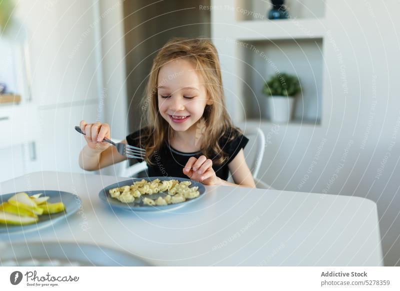 Happy preschool girl eating pasta at table child nutrition nourish smile food kid happy nutrient childhood plate content cute lunch charming dish appetite