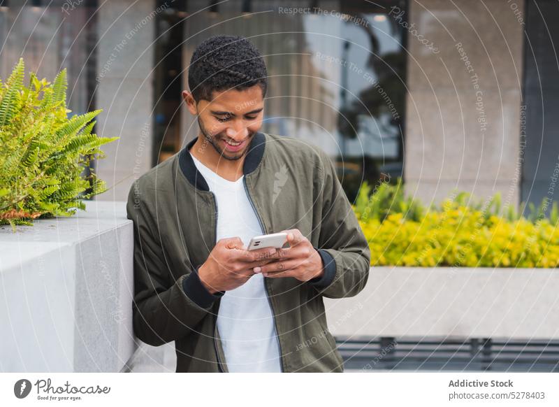 Happy ethnic man browsing smartphone on street using smile concentrate text message delight glad surfing male happy gadget latin device mobile connection