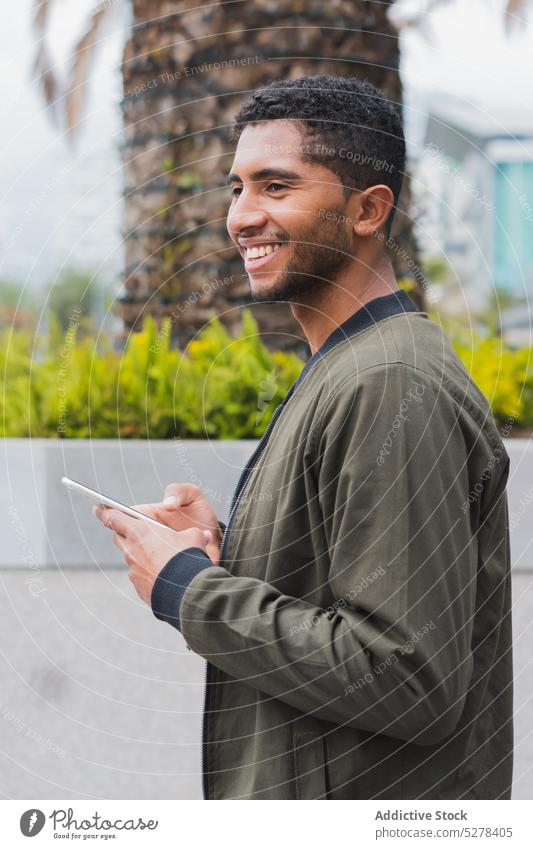 Happy ethnic man browsing smartphone on street using smile concentrate text message delight glad surfing male happy gadget latin device mobile connection