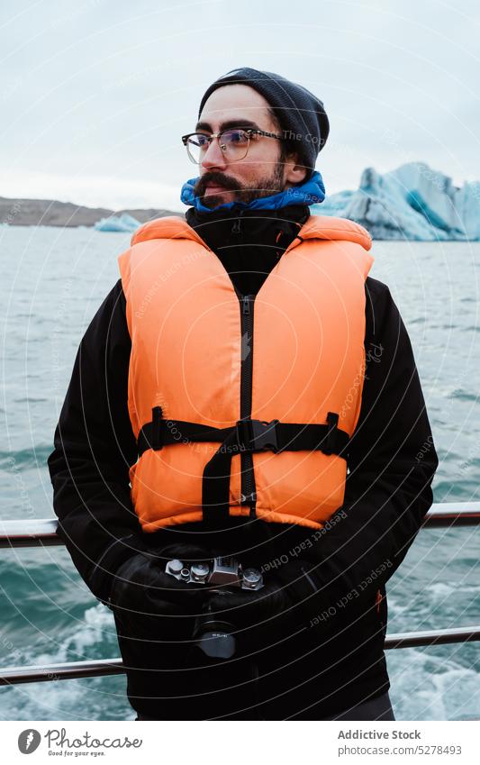 Male photographer on ship in sea man winter photo camera trip cloudy cold travel iceland shore outerwear vessel life jacket ocean sky overcast weather water