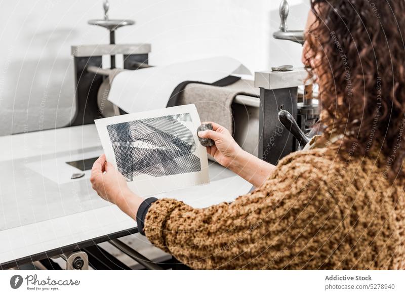 Anonymous female artisan inspecting engraved photos craftswoman examine photoengraving paper handmade table studio mature workshop hobby handicraft professional