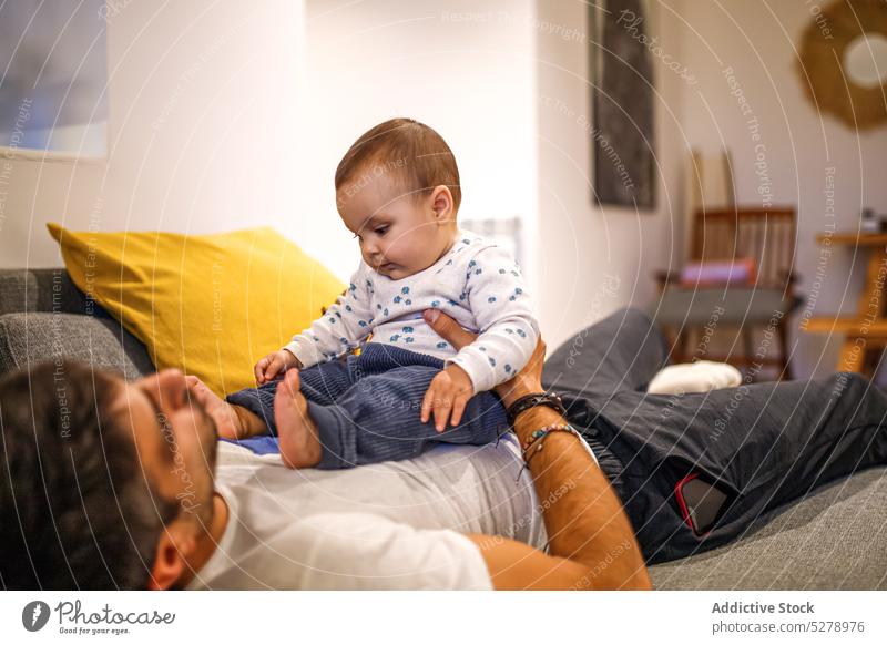 Smiling man playing cute baby on couch father happy toddler sofa home smile lying love weekend together child parent kid cheerful joy affection rest tender
