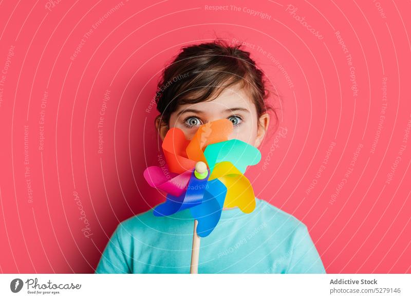 Funny girl with rainbow pinwheel kid carefree childhood funny playful toy cover face amazed personality expressive colorful cute vivid gaze stand blue eyes