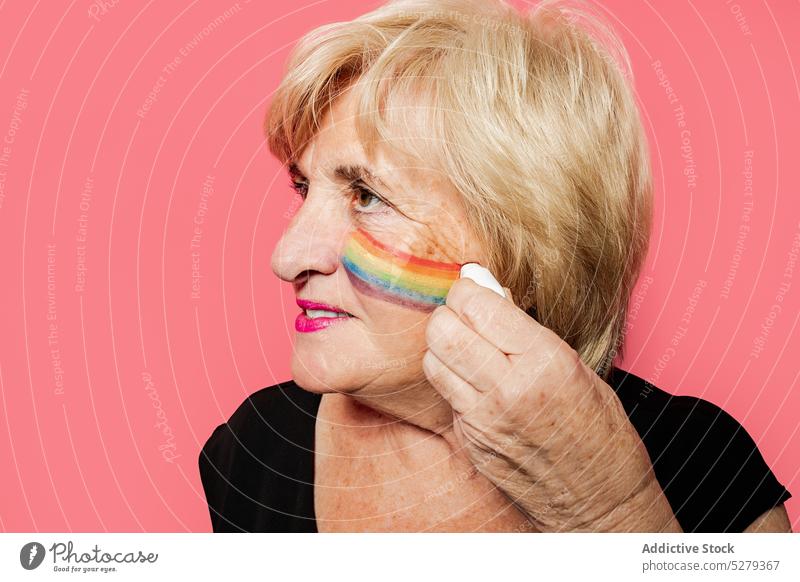 Elderly woman drawing rainbow on face portrait colorful positive creative bright smile paint happy retire art cheerful pensioner elderly senior female aged