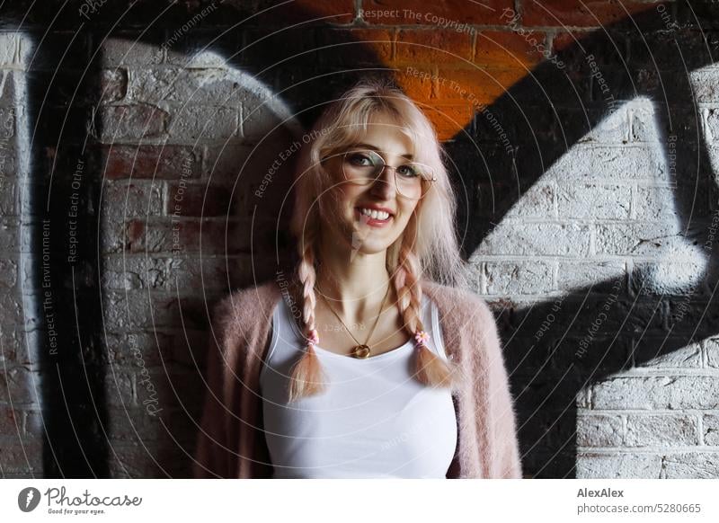 Young woman with pink blonde hair stands smiling in front of brick wall defaced with graffiti Woman Brick Wall (building) Graffiti portrait Eyeglasses pretty