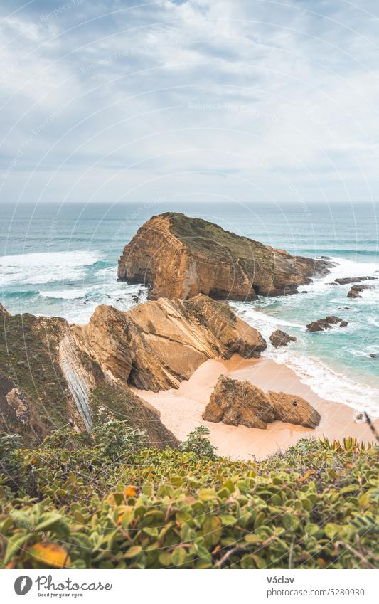 Steep cliffs plunging into the yellow-orange sand watered by the waves of the Atlantic Ocean in the region of Odemira, Portugal. In the footsteps of the Fisherman Trail, Rota Vicentina