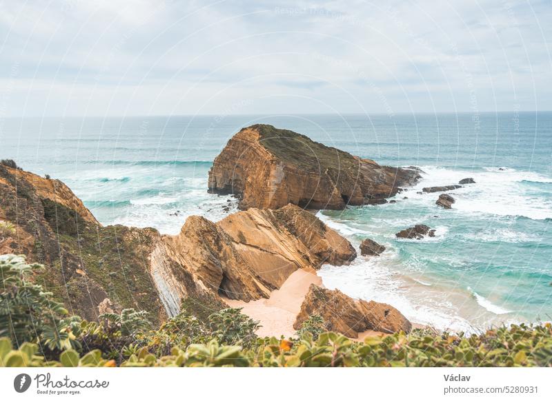 Steep cliffs plunging into the yellow-orange sand watered by the waves of the Atlantic Ocean in the region of Odemira, Portugal. In the footsteps of the Fisherman Trail, Rota Vicentina