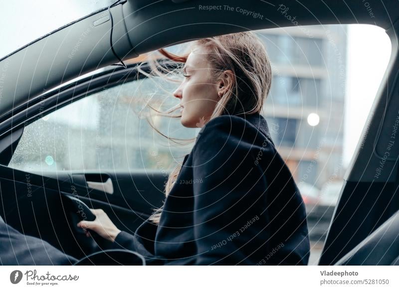 Woman in black coat get out from the car in the city. Windy weather, blowing hairs women wind taxi travel journey lifestyle relaxation outdoors freedom female