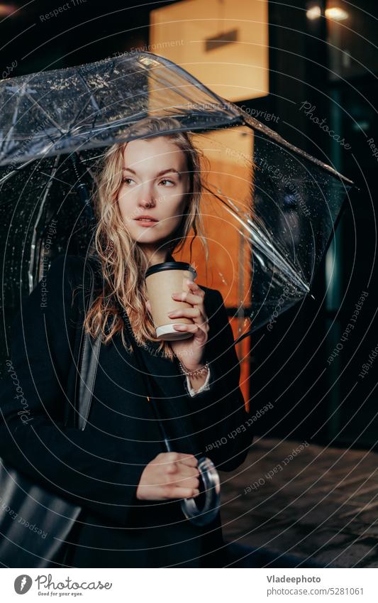 Blonde Woman in Coat Walking Under Umbrella and Holding Paper Cup in City umbrella woman cup rain holding standing paper weather autumnal coffee coat under