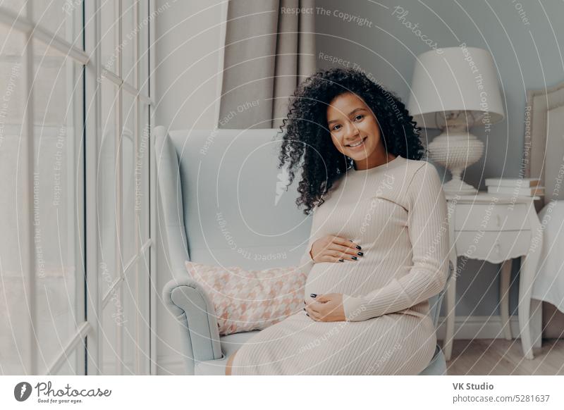 Positive pregnant woman touching gently her belly and smiling african mixed race young happy baby love child abdomen maternity mom mother motherhood parent