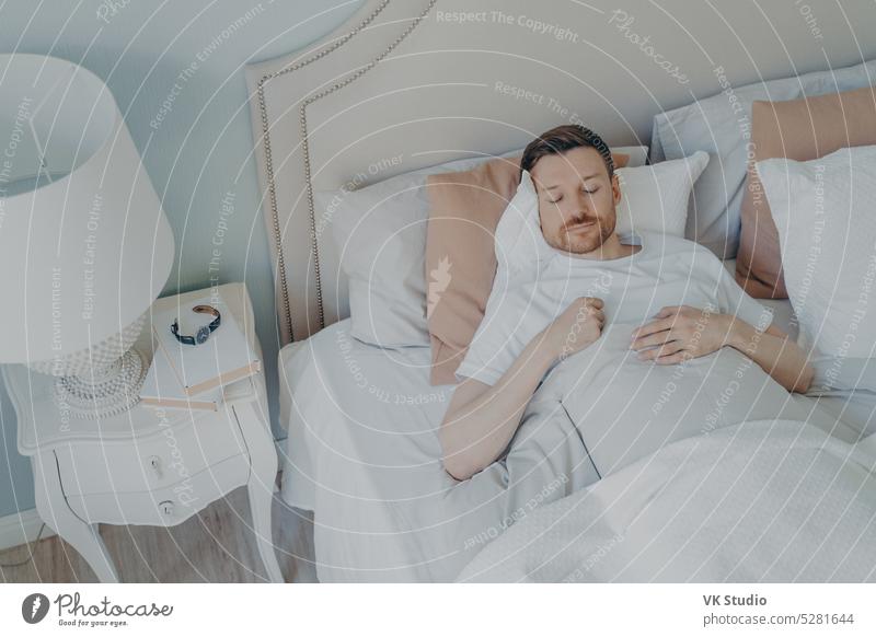 Handsome young bearded man sleeping in spacious comfortable bed nap morning bedroom cozy happy handsome bedding relax peaceful home asleep indoors lying