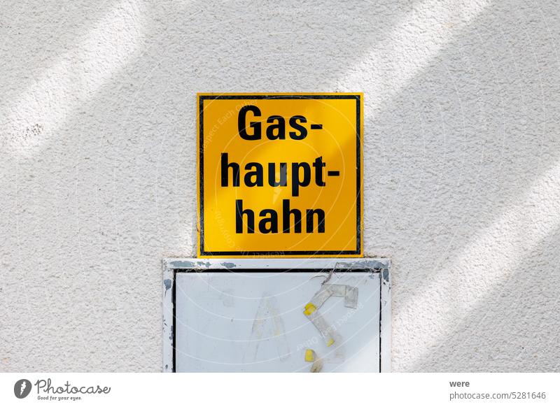 A yellow sign on a house wall with the German text Gas-haupt-hahn Main Check valve peril Emergency Fire department gas explosion Gas leak