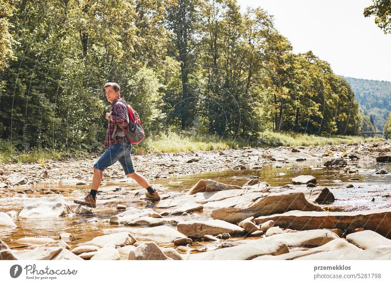 Trekking with backpack concept image. Backpacker wearing trekking boots crossing mountain river. Man hiking in mountains during summer trip adventure travel