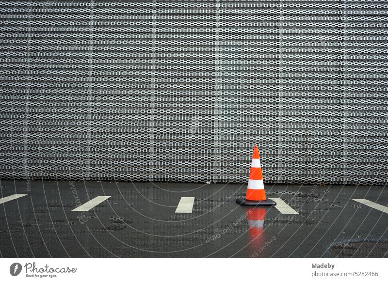 Lübeck hat, pylon or traffic cone in the rain on wet asphalt in front of the facade made of sheet steel of a modern car dealership in the Hanauer Landstraße in the Ostend of Frankfurt am Main