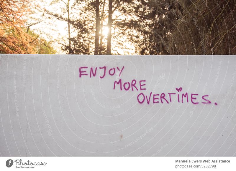 The sun rises behind a concrete wall. The wall reads, "Enjoy more overtimes." Wall (barrier) Concrete wall saying overcome work Stress Company hussle culture