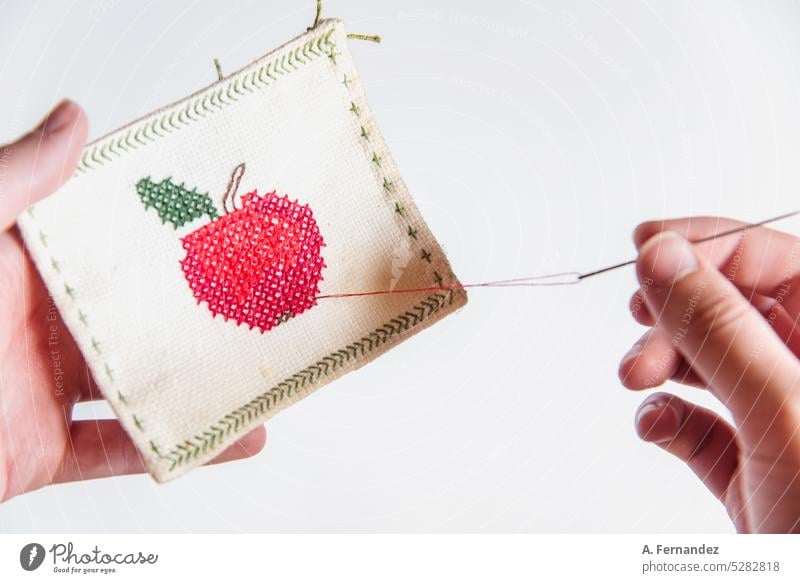 Detail of a hand holding a needle, embroidering an apple's design on a square piece of fabric. Cloth coaster sew Embroidery embroidered embroidery hoop fabricc