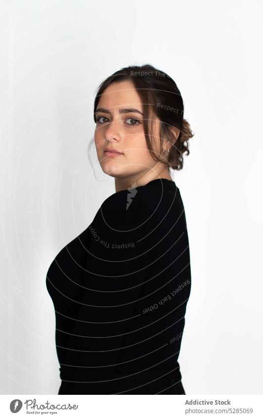 Woman in black outfit standing near white wall woman unemotional complexion emotionless simple profile calm serious hairdo sweater appearance thoughtful