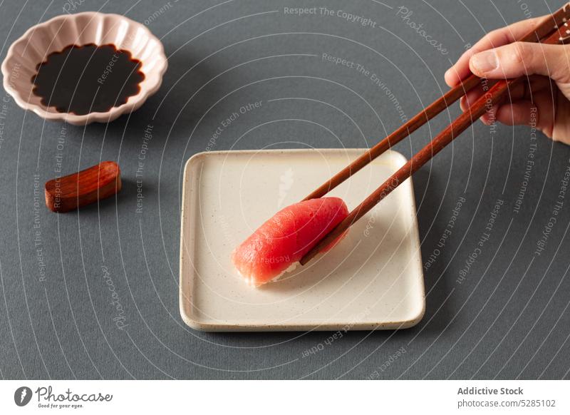 Crop person with chopsticks eating sashimi sushi hand plate soy sauce asian food serve cuisine oriental restaurant fish salmon handmade product delicious