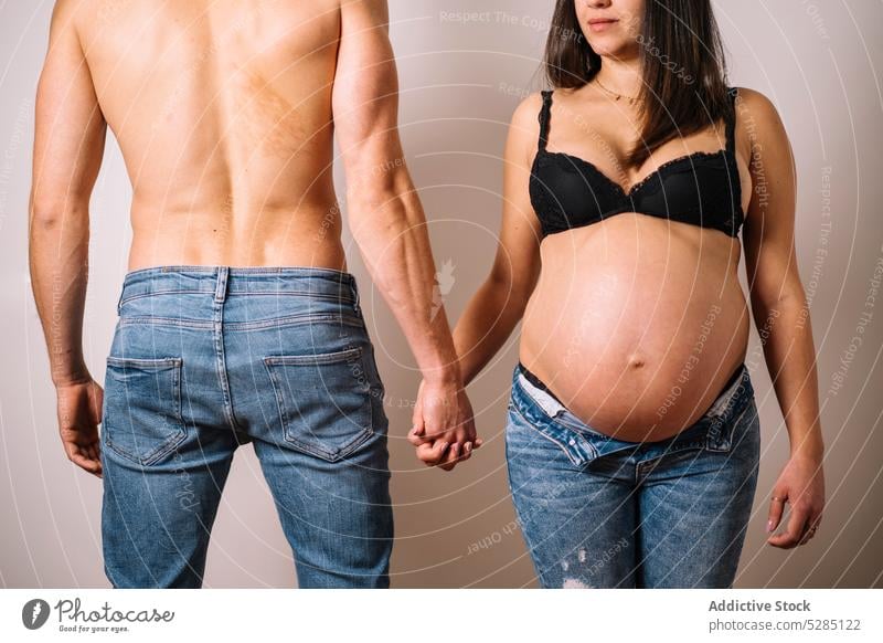 Pregnant woman holding hands with man couple husband pregnant wife shirtless lingerie pregnancy love maternal relationship belly bonding touch expect affection