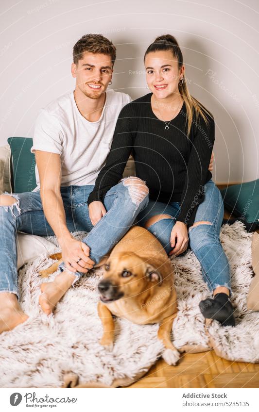 Happy couple sitting on floor with dog cuddle hug plaid pet animal domestic love bonding positive funny young canine home partner owner idyllic rest purebred