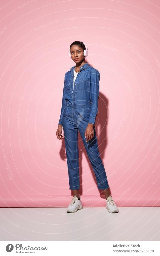 Fashionable black woman in denim outfit on pink background headphones listen style music model fashion trendy modern female ethnic african american young