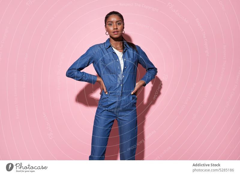 Confident black woman in denim outfit looking at camera in studio confident serious hand on waist model posture photo shoot pose young female african american