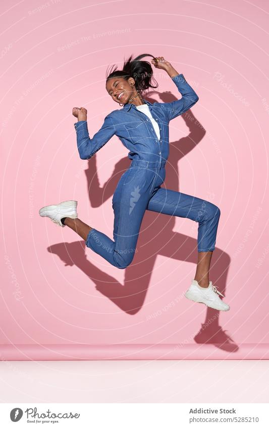 Happy black woman jumping high on pink background happy positive having fun cheerful excited trendy smile style arms raised female young african american joy