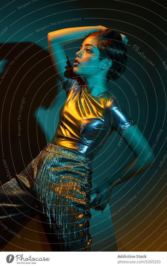 Stylish woman in shiny outfit in dark studio sensual trendy sequin model appearance fashion style vogue spangle pose short hair confident wall hairstyle shirt