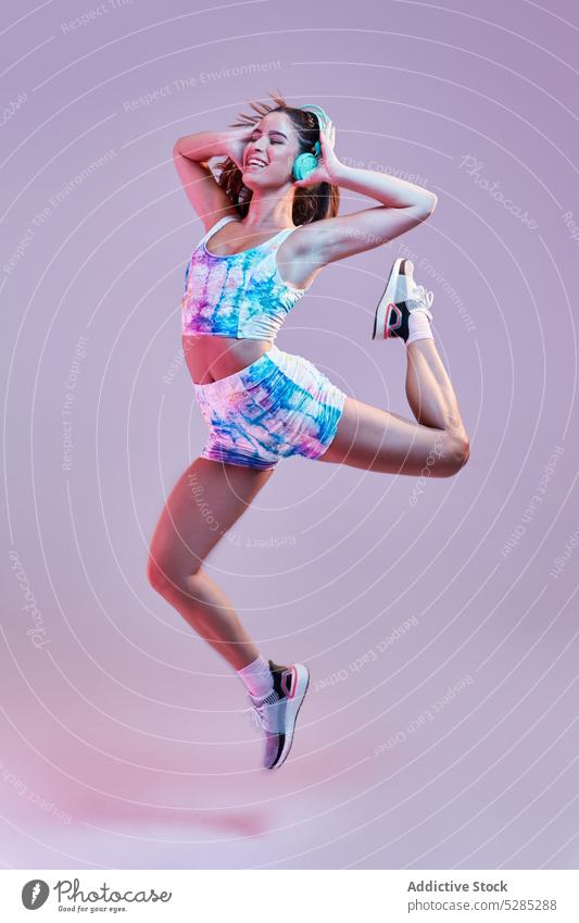 Woman jumping while listening to music on headphones woman dance energy motion touch studio shot female meloman tune sound young healthy lifestyle activewear