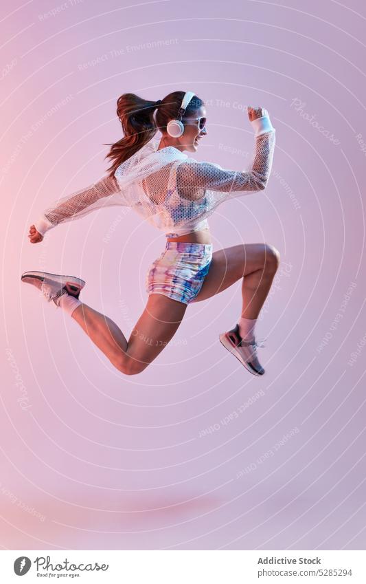 Fit woman in sportswear and headphones jumping up athlete style energy active fitness listen music workout happy colorful training motion female healthy