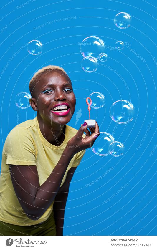 Delighted black woman blowing bubbles in studio makeup smile soap bubble style colorful trendy bright happy female african american vivid cheerful positive joy